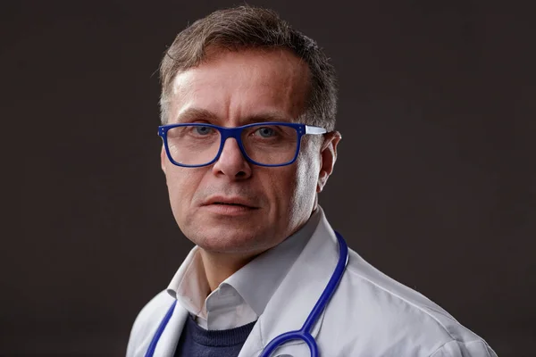 中年男子医生或护士戴眼镜和听诊器 在深色背景下带着极度关切的表情看着照相机 — 图库照片