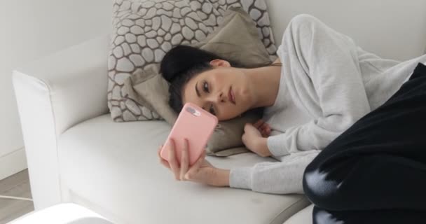 Ung kvinna som ligger i sin soffa och tittar på mobilens display — Stockvideo