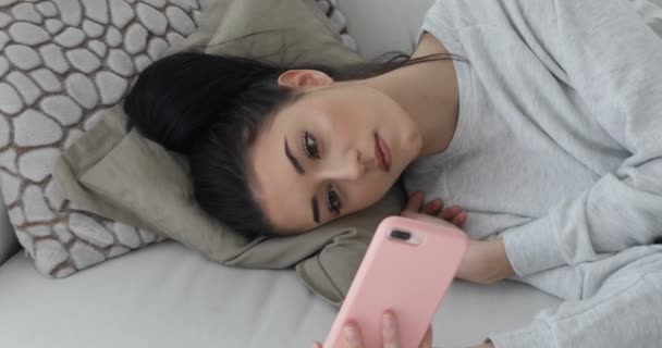Молодая женщина на диване с розовым смартфоном - видеоролик — стоковое видео