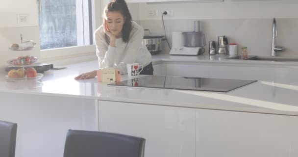 Chica viendo algunos videos en su teléfono inteligente rosa en la cocina — Vídeos de Stock