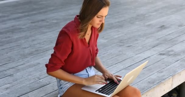 Young woman writing outside on a laptop in shorts — Stockvideo