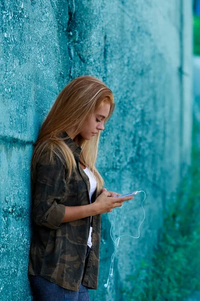 郊外の街のコンクリートの壁にもたれてスマートフォンを使う彼女はとても美しく不注意でソーシャルネットワークを使っているかもしれません — ストック写真