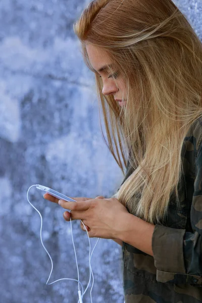 郊外の街のコンクリートの壁にもたれてスマートフォンを使う彼女はとても美しく不注意でソーシャルネットワークを使っているかもしれません — ストック写真