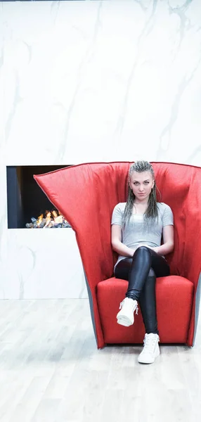 vaguely evil-looking girl waits in a slightly creepy red armchair