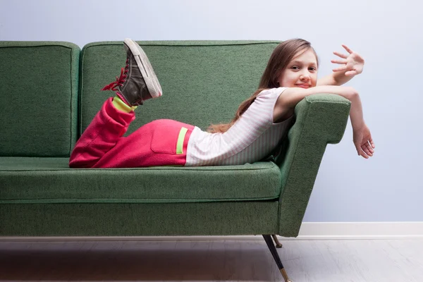 Niña saludando a la cámara tumbada en un sofá verde — Foto de Stock