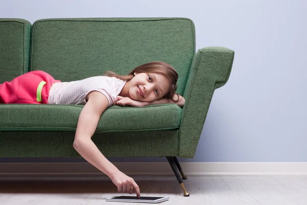 Menina usando um tablet relaxado em um sofá — Fotografia de Stock