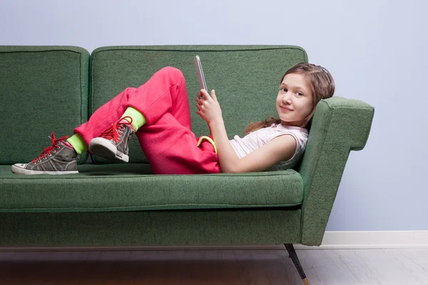 彼女のソファー上でタブレットを楽しむ少女 — ストック写真