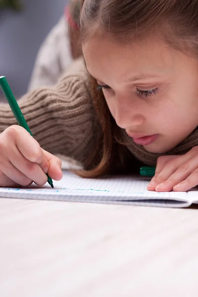 Kleines Mädchen schreibt konzentriert an ihrem Schulheft — Stockfoto