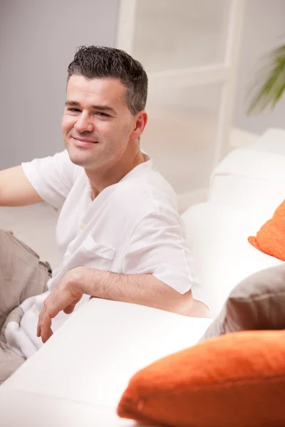 Ember mosolyogva a kamera a nappaliban pihentető — Stock Fotó