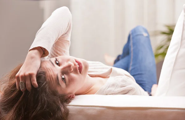 Pretty girl in blue jeans watching you from a sofa — Stock Photo, Image