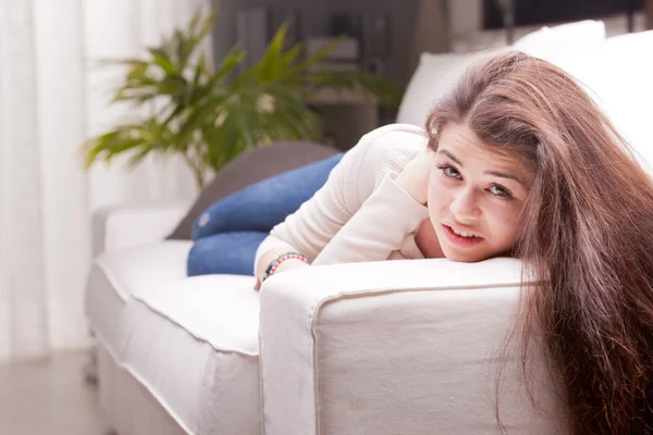 Menina bonita em jeans azul assistindo você de um sofá — Fotografia de Stock