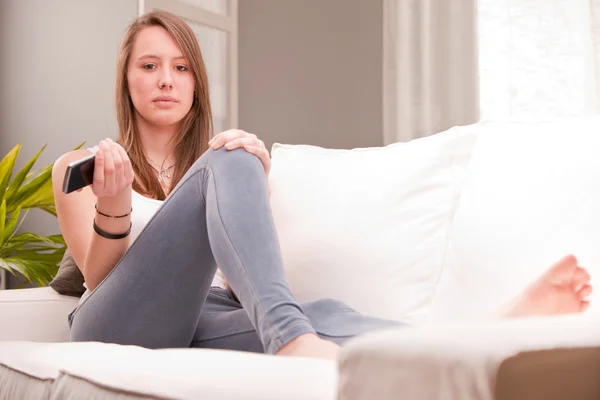 Ernste sexy Mädchen mit einem Handy auf einer Couch — Stockfoto