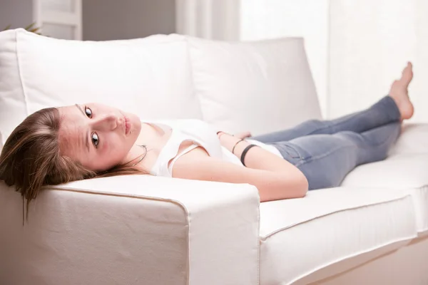 Ragazza guardando voi e sorridente mentre sdraiato su un divano — Foto Stock