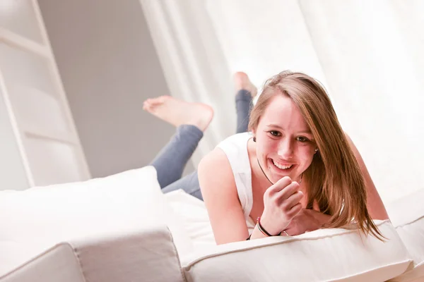 Menina sorridente em uma posição estranha em um sofá — Fotografia de Stock