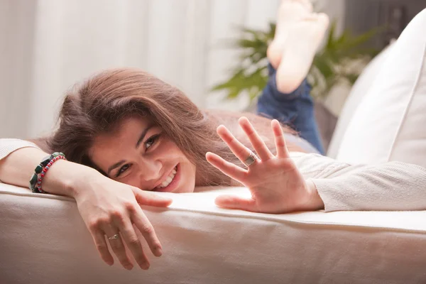 Jonge vrouw liggen op een sofa zwaaien bij ons — Stockfoto