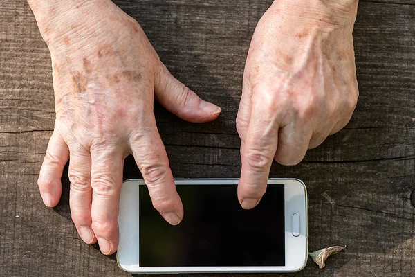 Mãos envelhecidas usando a tela sensível ao toque de um celular — Fotografia de Stock