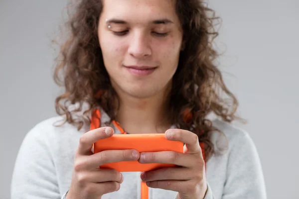 Langharige jonge man met een oranje smartphone — Stockfoto