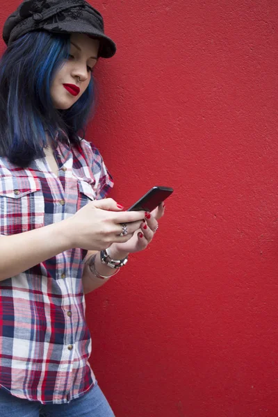 Hipster woman with mobile phone on red wall — Stock Photo, Image