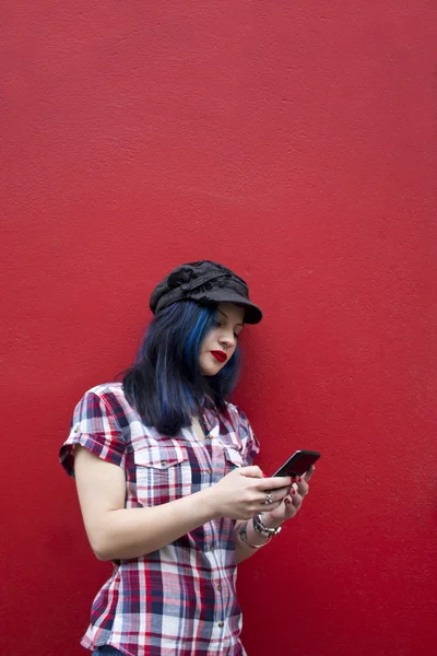 Hipster woman with mobile phone on red wall — Stock Photo, Image