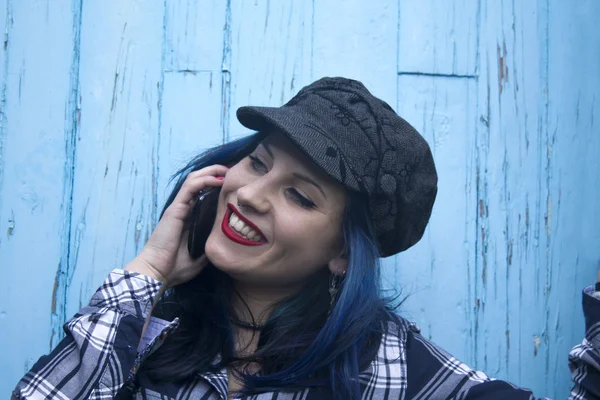 Хипстерская девушка разговаривает по мобильному телефону на синем фоне — стоковое фото