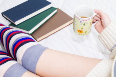 Kitaplarla yatıp kahve içen bir kadın.