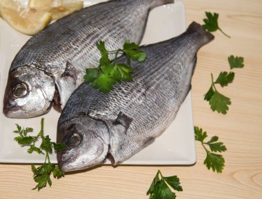 Maydanoz ve limonla kaplı tabakta taze çipura ya da çipura.