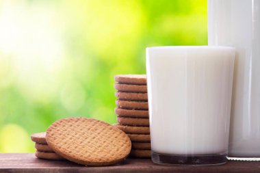 Arka planda bir bardak süt ve kurabiye.