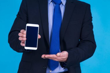 İş adamı mavi arkaplanda cep telefonu gösteriyor