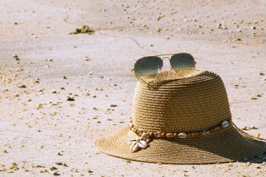 Şapka ve güneş gözlüğü. Beyaz kumda güneş koruması için plaj aksesuarları, mavi gökyüzü ve deniz arka planı, yaz tatili plajı.