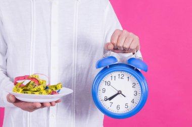 Adam elinde bant ve alarm saati, diyet ve sağlık konseptiyle tabak tutuyor.
