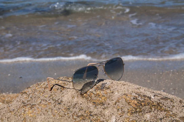 夏日沙滩上的蓝色太阳镜 背景为海浪 — 图库照片