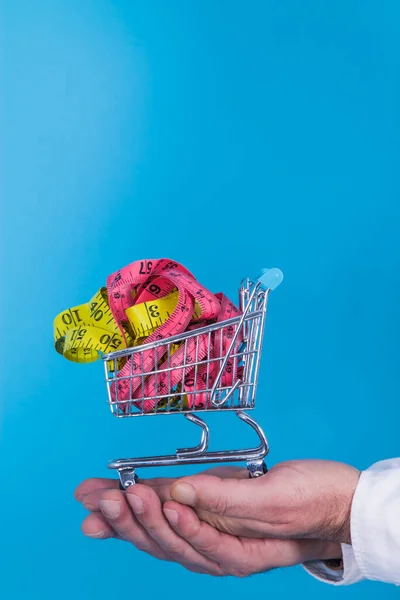 hands holding supermarket cart full of tape measures, diet and food concept