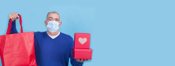 コロナウイルスやコヴィッド 19の顔に保護マスクをつけた魅力的な男ギフトボックス付きのコンセプトを提示します 誕生日やバレンタインデー — ストック写真