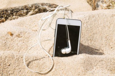 mobile phone with headphones in the sand on the beach