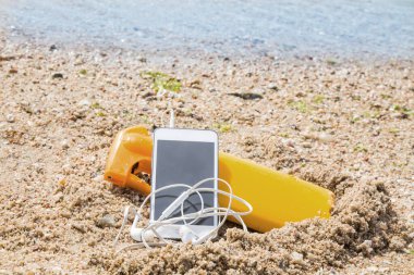 suntan lotion and mobile phone with headphones on the beach sand