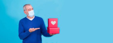 Koronavirüs ya da covid-19 için yüzünde koruyucu maskesi olan çekici bir adam ve hediye kutularıyla birlikte mevcut konsepti. Doğum günü ya da Sevgililer Günü