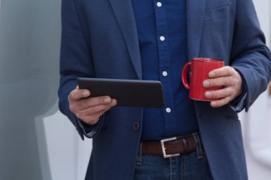 Takım elbiseli adam kahve içerken dijital tablet kullanıyor.