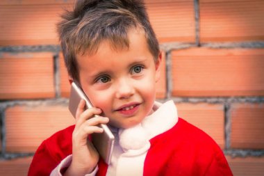 Mutlu gülümseyen çocuk Noel Baba kostümlü ve cep telefonlu.