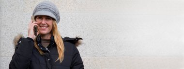 Akıllı telefonuyla duvara yaslanan gülümseyen kadın.