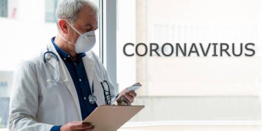 Cep telefonu kullanan maskeli bir doktor