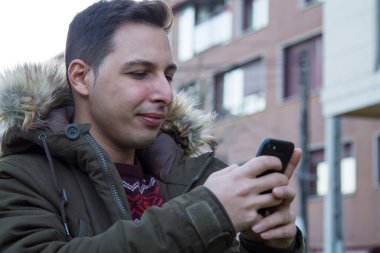 Gülümseyen adam sokakta akıllı telefon kullanıyor.