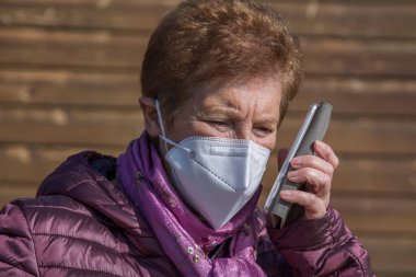 Maskeli ve tek kullanımlık tıbbi eldivenli cep telefonu kullanan yaşlı bir kadın. Koronavirüs salgını sırasında güvenlik önlemleri