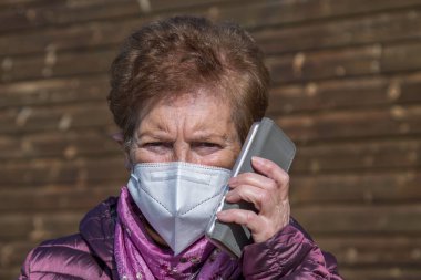 Maskeli ve tek kullanımlık tıbbi eldivenli cep telefonu kullanan yaşlı bir kadın. Koronavirüs salgını sırasında güvenlik önlemleri