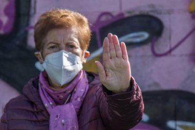 Tıbbi maskeli yaşlı bir kadın, dur ya da reddet tabelasını telif hakkı olmayan duvar yazısıyla asıyor.