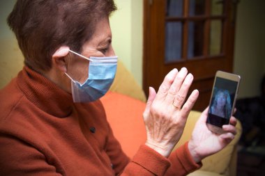 Korunaklı yüz maskesi takan yaşlı kadın Coronavirus salgını sırasında ailesiyle görüntülü görüşme yapıyor.