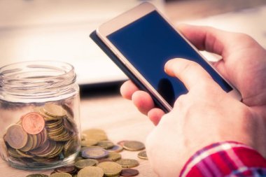 Adam cep telefonu ve para kavanozu kullanıyor, ekonomi ve tasarruf kavramı
