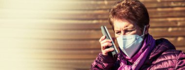 Maskeli ve tek kullanımlık tıbbi eldivenli cep telefonu kullanan yaşlı bir kadın. Koronavirüs salgını sırasında güvenlik önlemleri