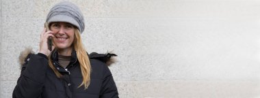 Akıllı telefonuyla duvara yaslanan gülümseyen kadın.