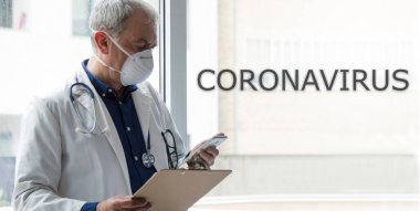 Cep telefonu kullanan maskeli bir doktor