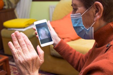 Korunaklı yüz maskesi takan yaşlı kadın Coronavirus salgını sırasında ailesiyle görüntülü görüşme yapıyor.